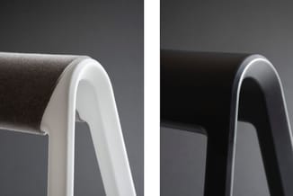 Detailweergave van twee stoelarmleuningen: links wit, rechts zwart, beide met grijze stofbekleding en afgeronde vormgeving.