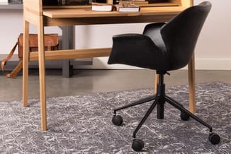 Houten bureau met zwarte bureaustoel op wielen, bruin leren tas, boeken en decoratie op blad, grijze tapijt.