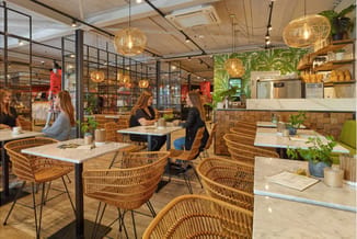 Modern kantoor met rieten stoelen, witte tafels, hangende gouden verlichting, groen accent wall, houten panelen en plantenacc