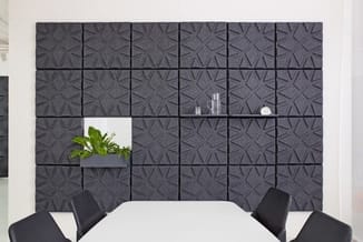 Vergaderruimte met witte ronde tafel, zwarte stoelen en grijze akoestische wandpanelen met geometrisch patroon en plantenlegg