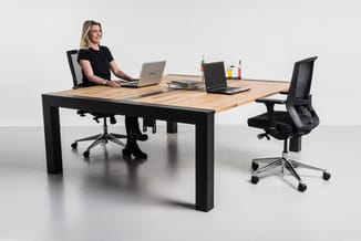 Houten vergadertafel met zwart onderstel, zwarte bureaustoelen met netrug, laptops en kantoorartikelen op het tafelblad in mo