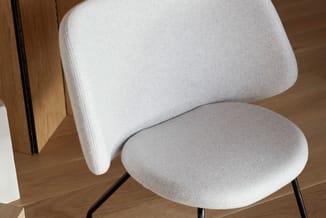 Moderne stoel met wit gestoffeerde zitting en rugleuning, zwarte metalen poten, op houten vloer tegen houtstructuur achtergro