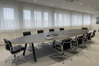 Moderne vergaderzaal met grijze ovale tafel, zwarte design stoelen, raampartij met wit gordijn en recessed lighting.