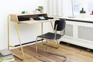 Minimalistisch bureau met geel metalen frame en lichte houten blad, zwarte organizer bovenop, zwarte kantoorstoel, in heldere