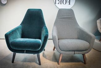 Twee fauteuils naast elkaar: links een turquoise velours fauteuil met zwarte poten, rechts een grijze structuurstof fauteuil