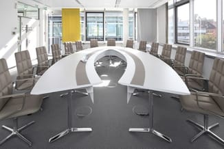 Moderne vergaderzaal met gebogen witte conferentietafel, grijze bureaustoelen, grote ramen en geel accent element aan plafond