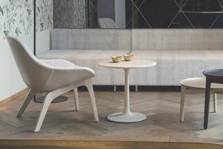 Moderne loungehoek met beige stofbank, witte kuipstoel, wit rond tafeltje en zwart bijzettafeltje op houten vloer.