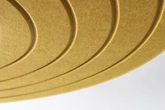 Gouden akoestische wandpanelen met gewelfde oppervlakte en donkere groeflijnen, gedeeltelijk zichtbaar tegen witte achtergron