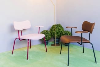 Twee designstoelen met rode en zwarte metalen frame en roze respectievelijk bruin leren zitting in groene showroomruimte met