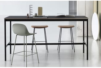 Zwarte statafel met twee houten barkrukken en één grijze stoel in minimalistisch kantoorinterieur.