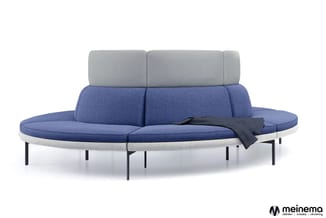 Ronde blauwe lounge bank met grijze rugkussens, lichtgrijze zitrand en zwarte metalen poten, zwarte deken erover.