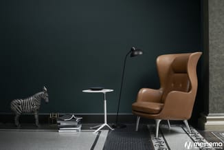 Bruinleren fauteuil met hoge rug en voetensteun in moderne kantoorruimte met donkergroen muur, witte bijzettafel, zwarte staa