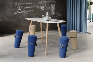 Vergaderruimte met ovale witte tafel op houten poten, omringd door blauwe en beige cilindervormige poefzit. Achter de tafel e