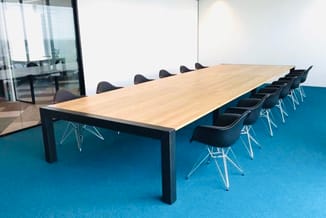 Moderne vergadertafel met licht houten blad en zwart metalen onderstel, omringd door zwarte stoelen met witmetalen poten op b