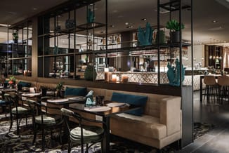 Moderne restaurant- of loungeruimte met beige zitbanken, zwarte stoelen, zwarte tafels, glazen scheidingswanden, bar met fles