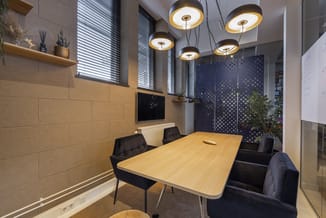 Moderne vergaderkamer met houten tafel, zwarte stoelen, beige wandpanelen, hangende zwart-gouden plafondlampen en donkerblauw
