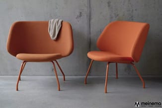 Twee oranje stoelen met afgeronde rugleuning en metalen poten tegen betonnen achtergrond. Links een stoel met beige doek over