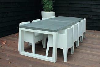 Witte vergadertafel met grijsgroene blad en zes bijpassende witte stoelen op houten terras, tegen donker houtwerk.