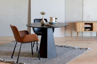 Moderne eetkamer met zwarte ronde tafel, cognackleurige stoel, houten dressoir, grijze tapijten en minimalistische inrichting
