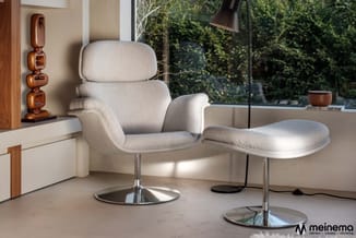 Beige loungestoel met ottoman op zilverkleurig voetsteuk in moderne kantoorruimte met raampartij, houten decoratieve element