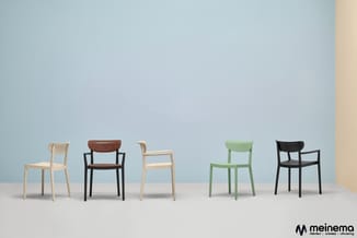 Vijf stoelen in verschillende kleuren en materialen tegen een blauwe wand: naturel hout, bruin leer, naturel hout, groen en z