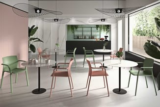 Modern caféruimte met ronde tafels, groene en roze stoelen, hangende zwarte draadluchters, planten en "LOUNGE café" tekstbord