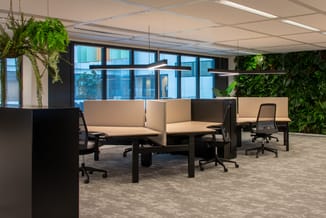 Modern kantoorlandschap met beige akoestische schermen, zwarte bureaus, ergonomische stoelen, hangende groene planten en grot