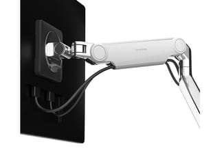 Humanscale monitorarm in zilver en zwart, gemonteerd op zwarte wand met kabelmanagement, verstelbaar voor ergonomische werkpl