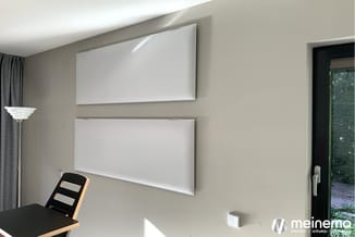 Twee witte whiteboards aan beige muur in kantoor, met zwart bureau en houten kastje, glazen deur naar buiten.