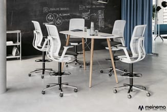 Moderne kantoorruimte met witte ergonomische bureaustoel op wielen rond een wit tafelblad met houten poten. Zwart memobord op
