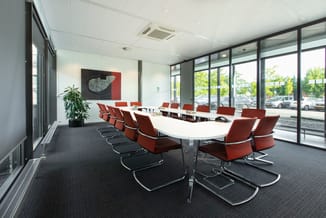 Moderne vergaderruimte met witte tafel, rode kantoorstoel met zwart frame, grijze vloerbedekking en grote glazen ramen met ui