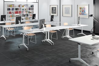 Modern kantoor met witte mobiele tafels, beige stoelen, zwarte tegelvloer, boekenkast achteraan en drie ingelijste kunstwerke