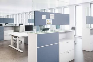 Modern open kantoor met witte bureaus, blauwe scheidingswanden, ergonomische stoelen en grote ramen. Monitoren en documenten