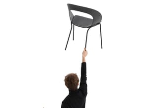 Man houdt zwarte designstoel met gebogen rugleuning en metalen poten omhoog tegen witte achtergrond.