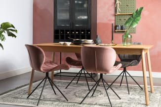 Eettafel van licht hout met vier roze stoelen met zwarte pootjes, zwarte kast met glazen deuren op roze muur, groene pegboard