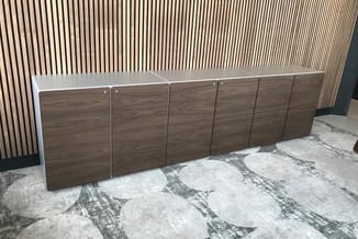 Modulaire houten kasten met witte bovenbladding, zes deuren in donker houtfineer, opgesteld tegen verticale wandpanelen in ka