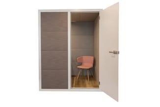 Kleine akoestische werkcel met grijsbruine wanden, glazen deur en houten vloer. Roze stoel met houten poten binnenin.