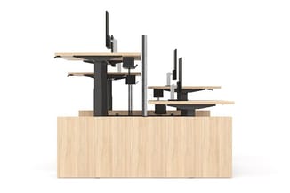 Twee ergonomische zit-sta bureaus met zwart metalen frame en houten bladen op houten werkblad, monitonarmen met zwarte scherm