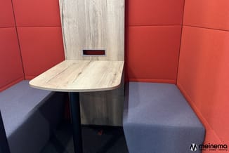 Belcel met rode akoestische zijwanden, grijsblauwe zitbanken, licht houten tafel en achterwand met mailslot.
