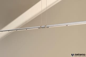 Hangende lineaire LED-verlichting in zilver met gouden ophanging tegen beige plafond en wand.