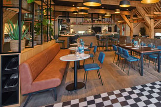 Modern kantoor met oranje ribfluwelen zitbank, blauwe stoelen, ronde tafel, houten balken, parketvloer en zwart-wit tegels.