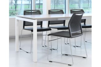 Witte vergadertafel met zwarte stapelstoelen met perforeerde rugleuning en zilveren onderstel in moderne kantoorruimte.