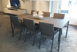 Moderne vergadertafel met grijze blad en donkergrijze stoelen in kantoorruimte met ramen en inbouwkasten.