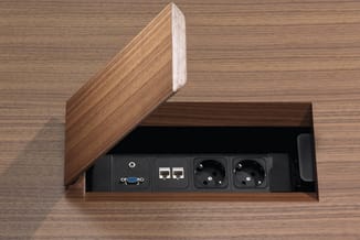 Houten bureauslot met open klep, bevattende VGA-aansluiting, netwerk-aansluitingen en twee stopcontacten op zwarte achtergron