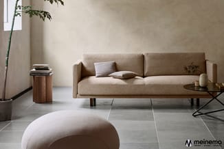 Moderne woonkamer met beige linnen sofa, ronde poef, houten bijzettafel, zwart metalen salontafel en bamboe plant tegen neutr