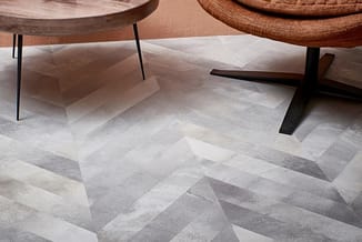 Twee ronde houten tafels met metalen poten op grijze geometrische vloer in visgraatpatroon.