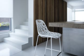 Witte opengewerkte designstoel aan houten bureau in modern kantoor met trap, bruine gordijnen en raam.