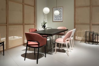 Vergadertafel met zwart blad en zwarte poten, omgeven door roze/koraalkleurige stoelen, hangende bollamp, houten schuifdeuren