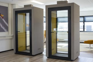 Twee gesloten belcellen met grijze buitenkant, geel/groen interieur en zwarte deurkozijnen in een modern kantoor.