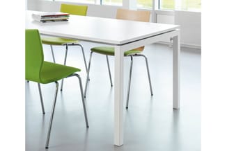Witte vergadertafel met groene stoelen met metalen poten in moderne kantooromgeving met ramen en stapel boeken op tafel.